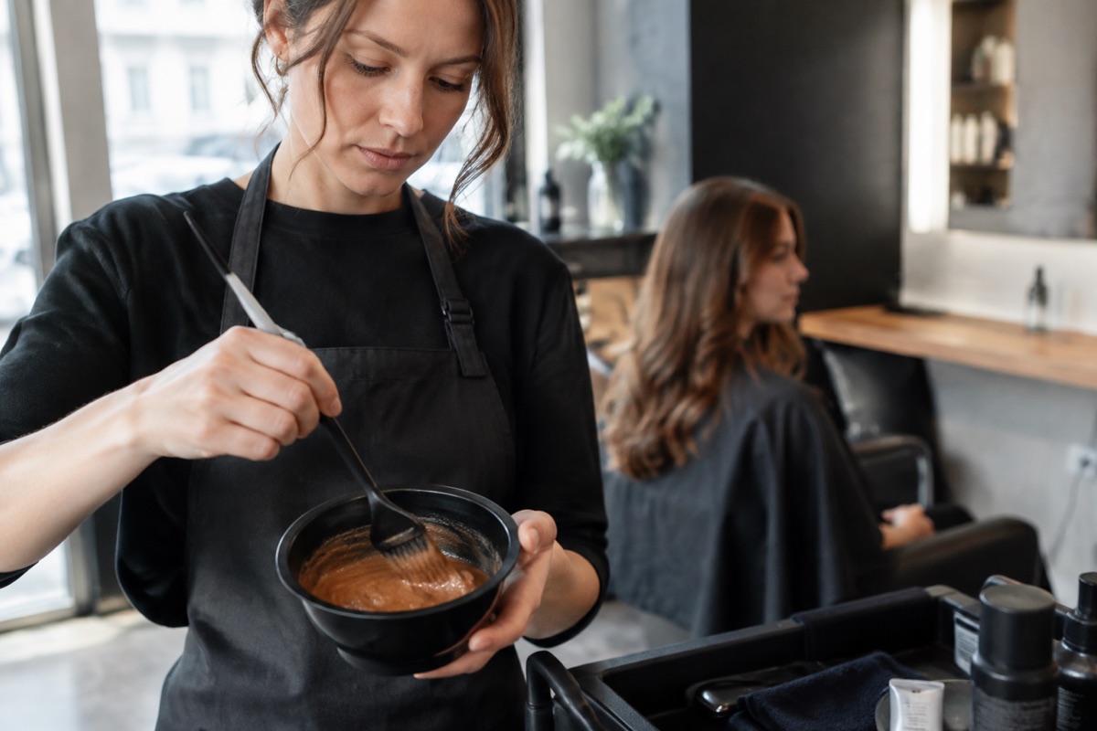 Friseur mischt Kastanienbraun-Farbe für eine Kundin im Salon