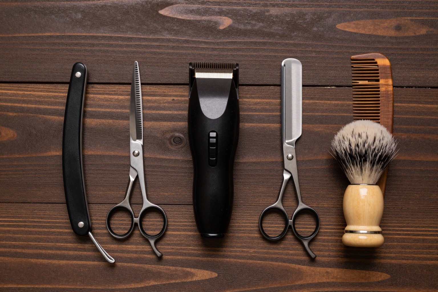 Flatlay mit Barbershop-Equipment: Rasiermesser, Schere, Trimmer, Rasierpinsel und Kamm auf Holz